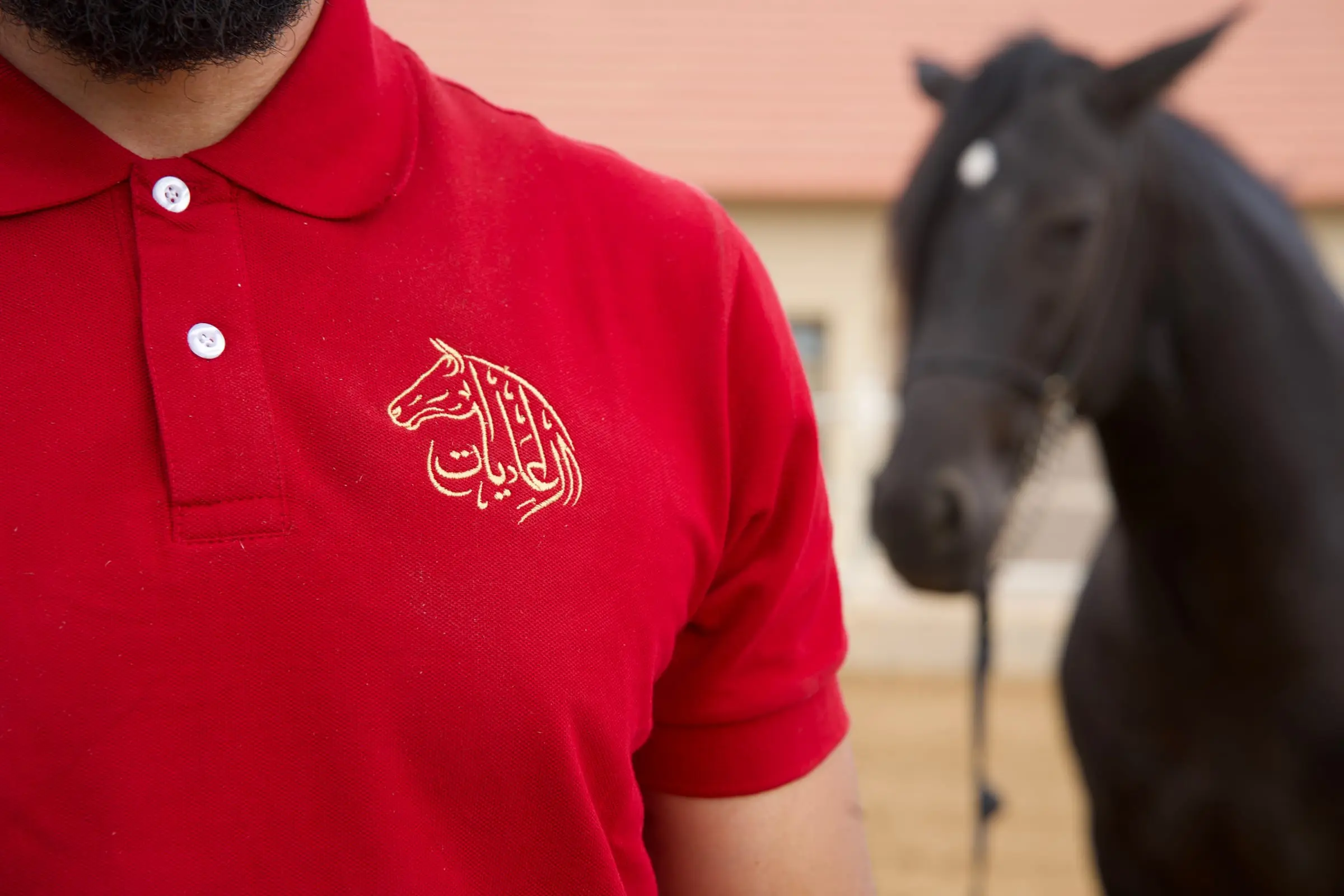 Polo rouge brodé du logo El Adiyat, porté par un palefrenier